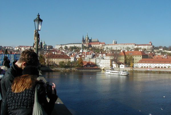 A river and in the background an historic city with a church on the top of a hill, surrounded by old buidlings.