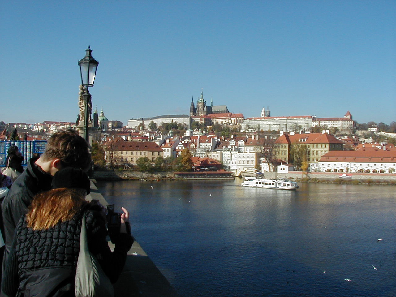 A river and in the background an historic city with a church on the top of a hill, surrounded by old buidlings.