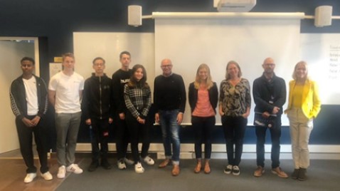 Students are standing in front of a class room with several adults, posing for the camera.