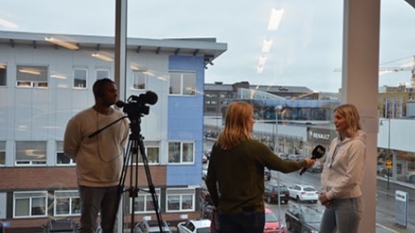 1 Person is interviewed by another, while a camera man is filming.