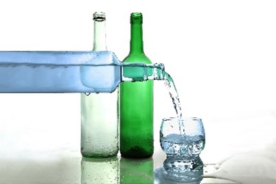 Water is being poured into a glass from a bottle with two more bottles standing behind it.