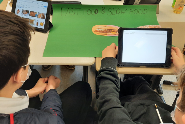 A group of students sit around a desk with tablets.