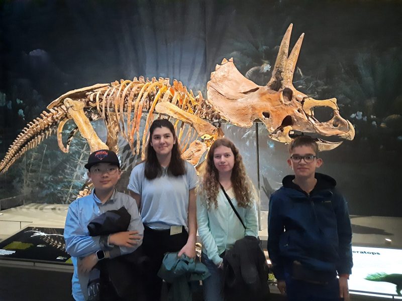 A group of students pose in front of a dinosaur skeleton at Naturalis Museum.