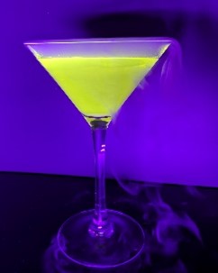 A glowing and steaming neon yellow cocktail in standing on a desk. The background is dark purple.