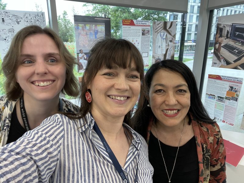 3 people with medium to long hair are smiling into the camera.